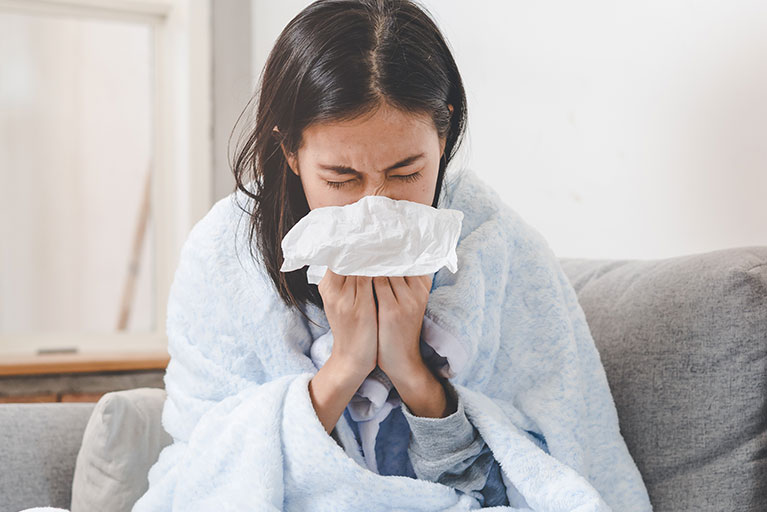 Frau auf der Couch mit Taschentuch: Erkältung oder Grippe