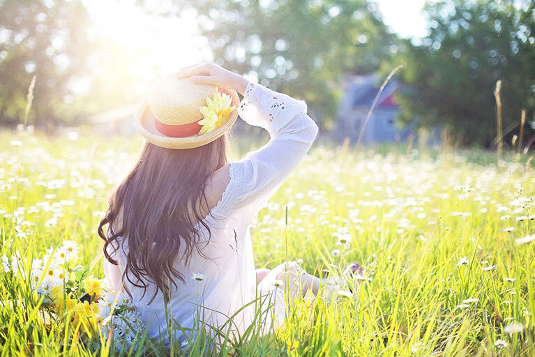 Frau mit Hut auf der Wiese bei Sonnenschein