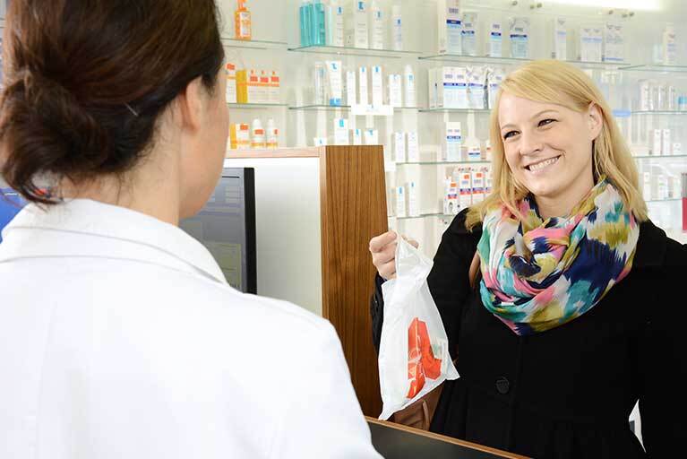 Frau mit Apotheken-Tasche am Counter in der Apotheke