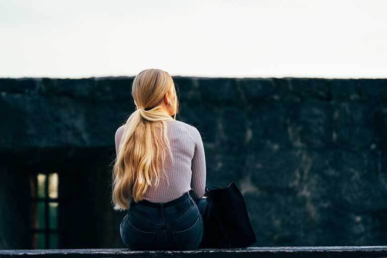 Frau sitzt mit dem Rücken zum Bild auf einem Tisch