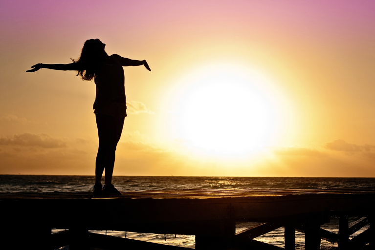 Frau mit geöffneten Armen bei Sonnenuntergang