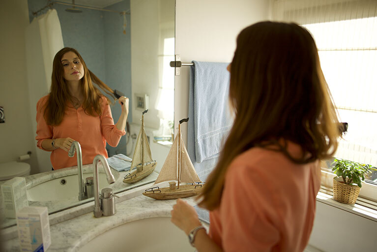 Frau schaut sich im Spiegel an während sie ihre Haare bürstet
