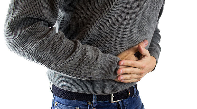 Ein Mann krümmt sich mit Magenschmerzen leicht nach vorne und presst beide Hände auf seinen unteren Bauch.